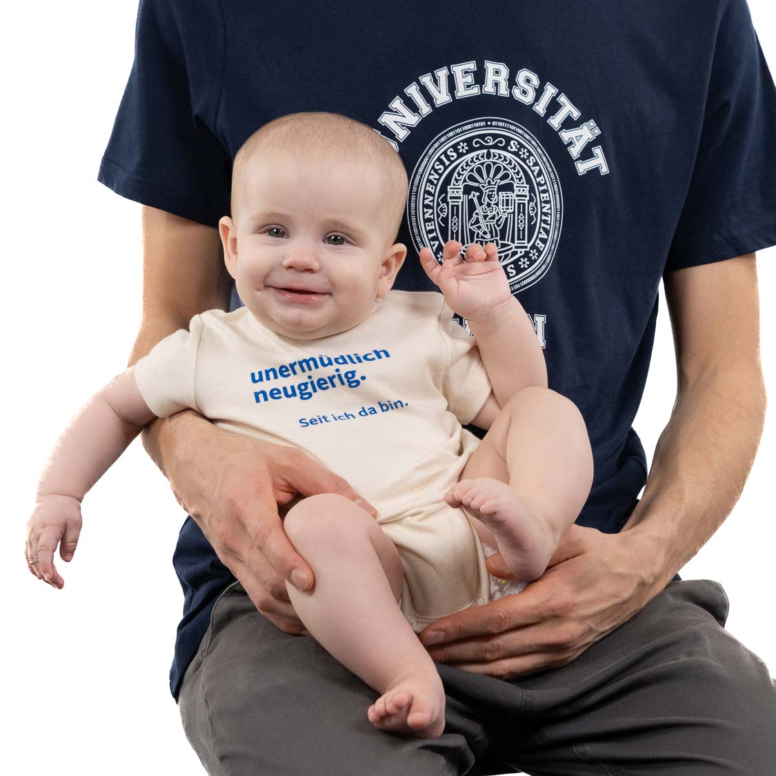 Baby-Body in Creme mit blauem Text „unermüdlich neugierig. Seit ich da bin.“; gehalten von Person im dunkelblauen Uni-Wien T‑Shirt.