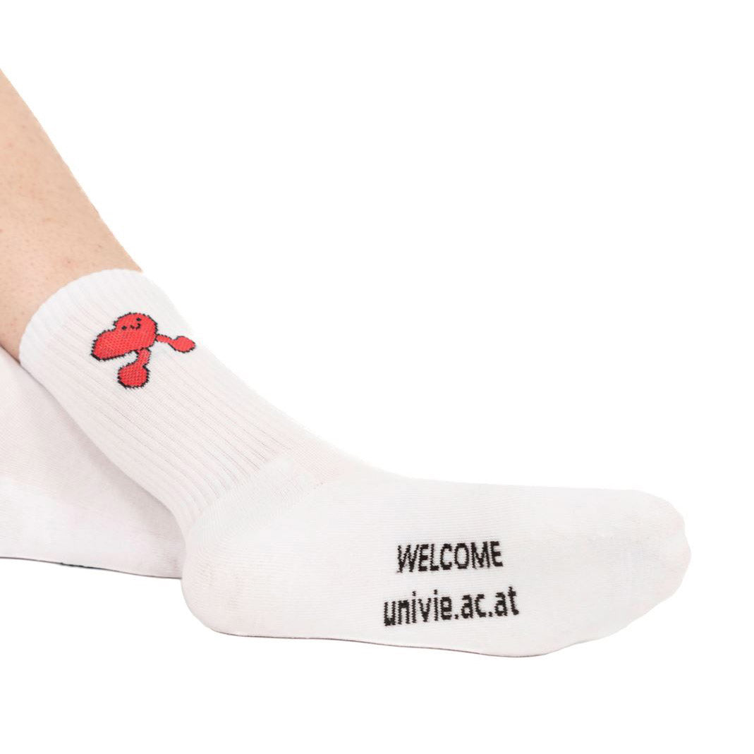 Weiße Sportsocken mit rotem Herz‑Motiv am Schaft; an der Fußsohle schwarzer Text „WELCOME univie.ac.at“.