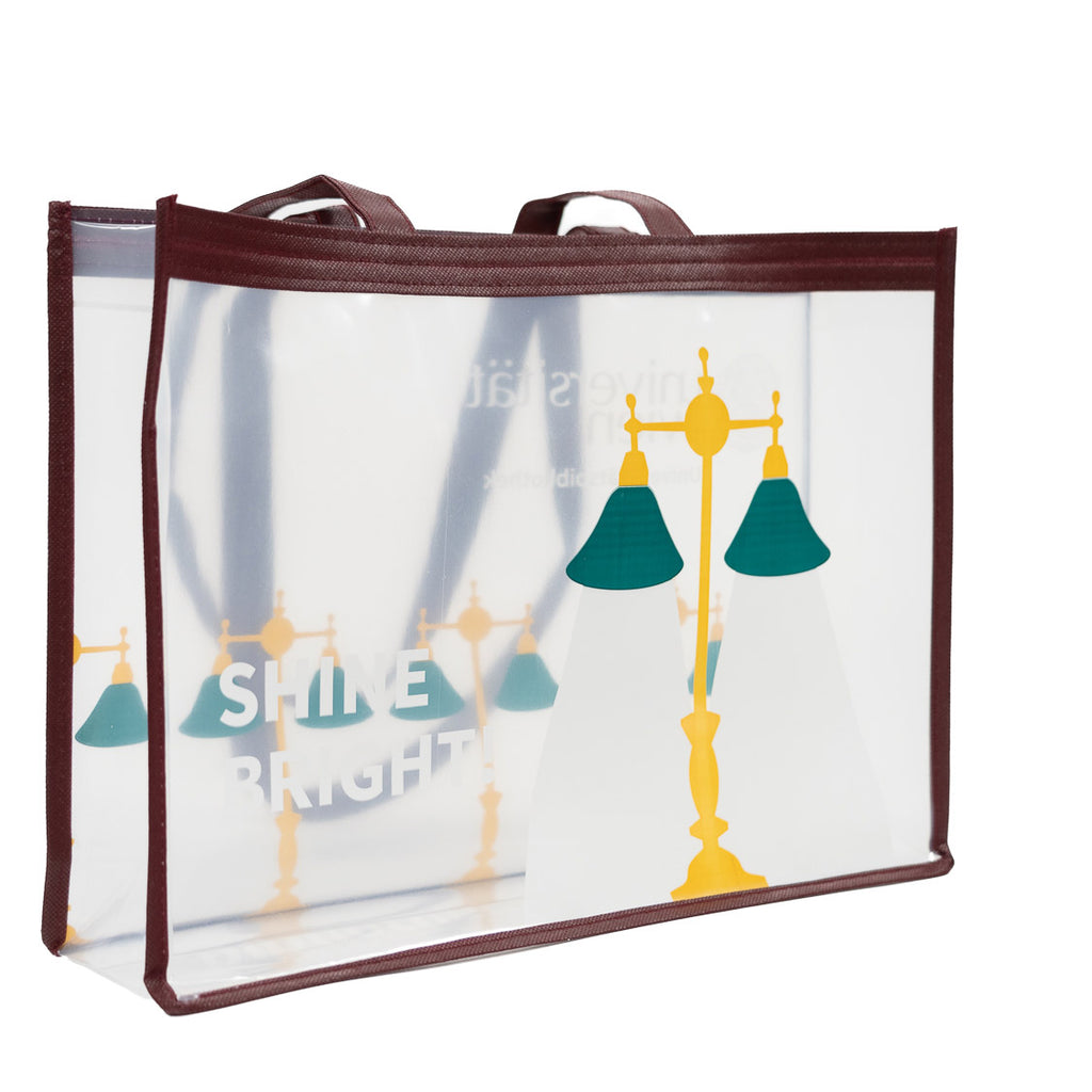Transparente Tragetasche mit bordeauxfarbenem Rand; Motiv mit gelb‑grünen Leselampen und dem weißen Schriftzug „SHINE BRIGHT!“.