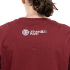 Rückansicht eines bordeauxfarbenen T‑Shirts. Am oberen Rücken ist in Weiß das Logo „Universität Wien“ mit Siegel aufgedruckt.